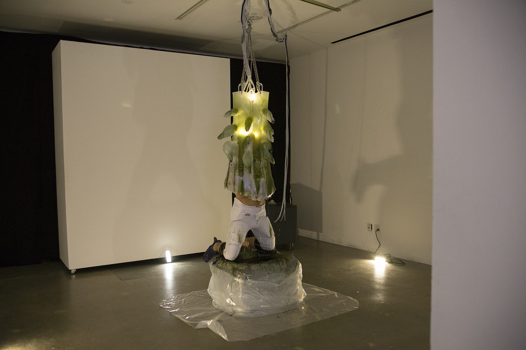 A man engulfed in a gelatenous form covered in tentacles knealing over a pool of green slime in a gallery